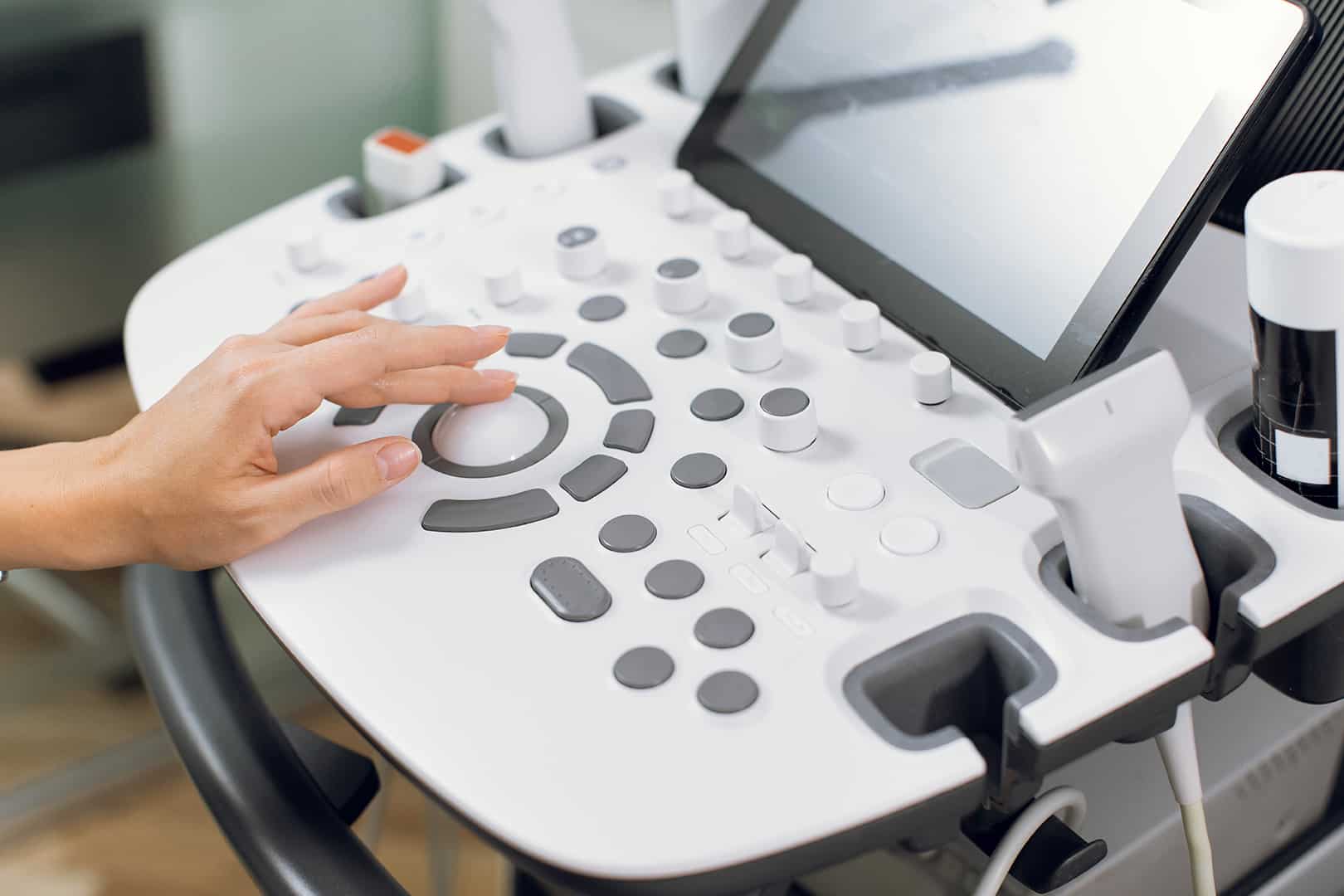 Close up cropped shot of modern medical device, ultrasound machine scanner at work. Hand of professional female doctor sonographer pushing buttons on ultrasound control panel